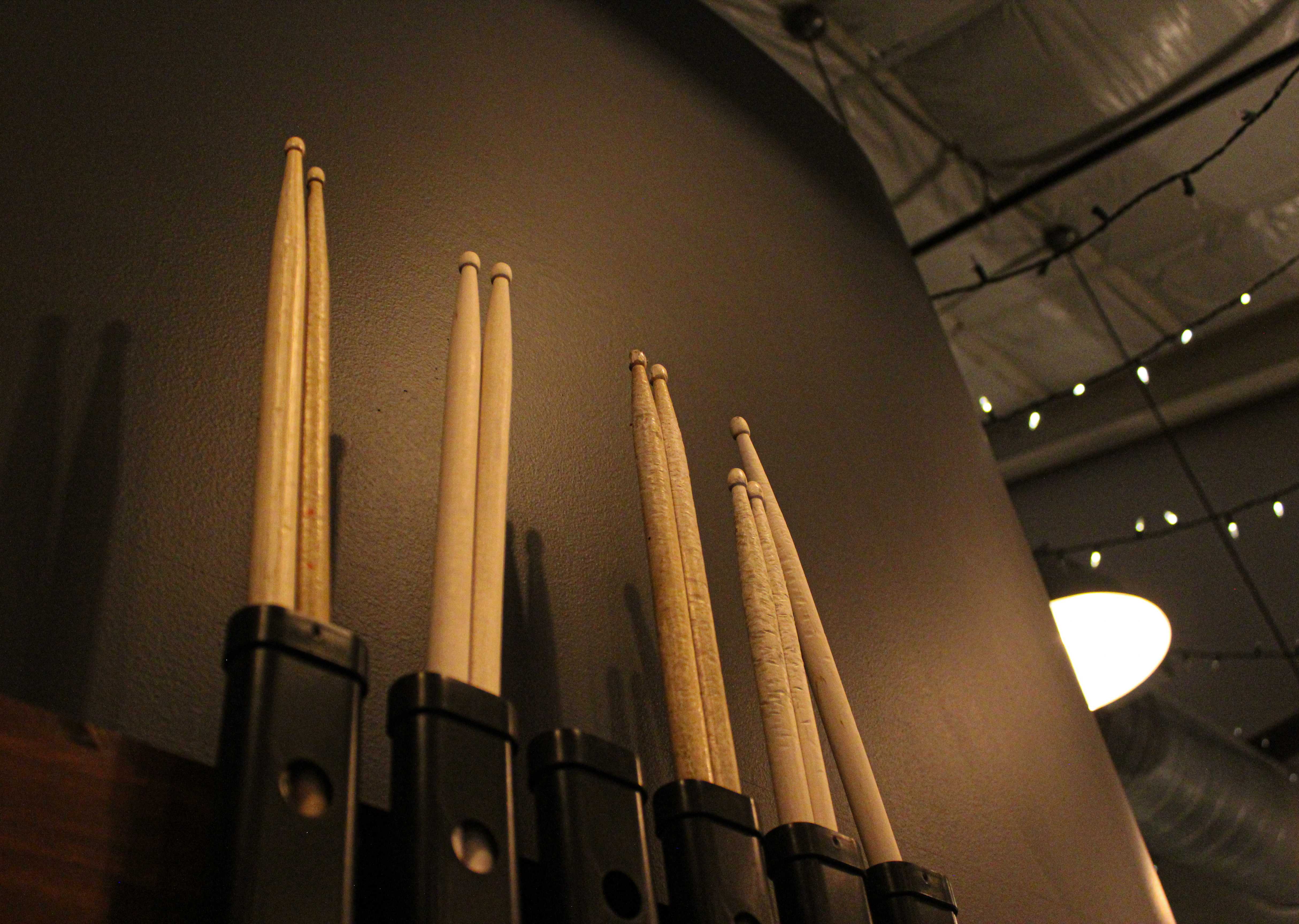 Spare drumsticks lined up in wall holders beneath string lights