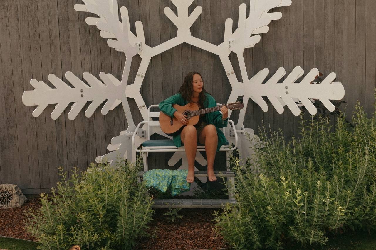 Kiley, founder of Soundcheck, playing guitar in front of a large wooden snowflake