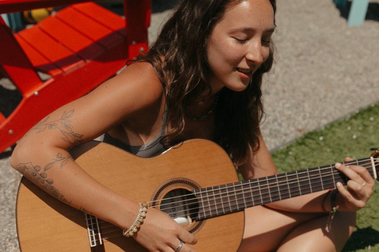 Kiley, founder of Soundcheck Practice Studios, playing an acoustic guitar in the sun