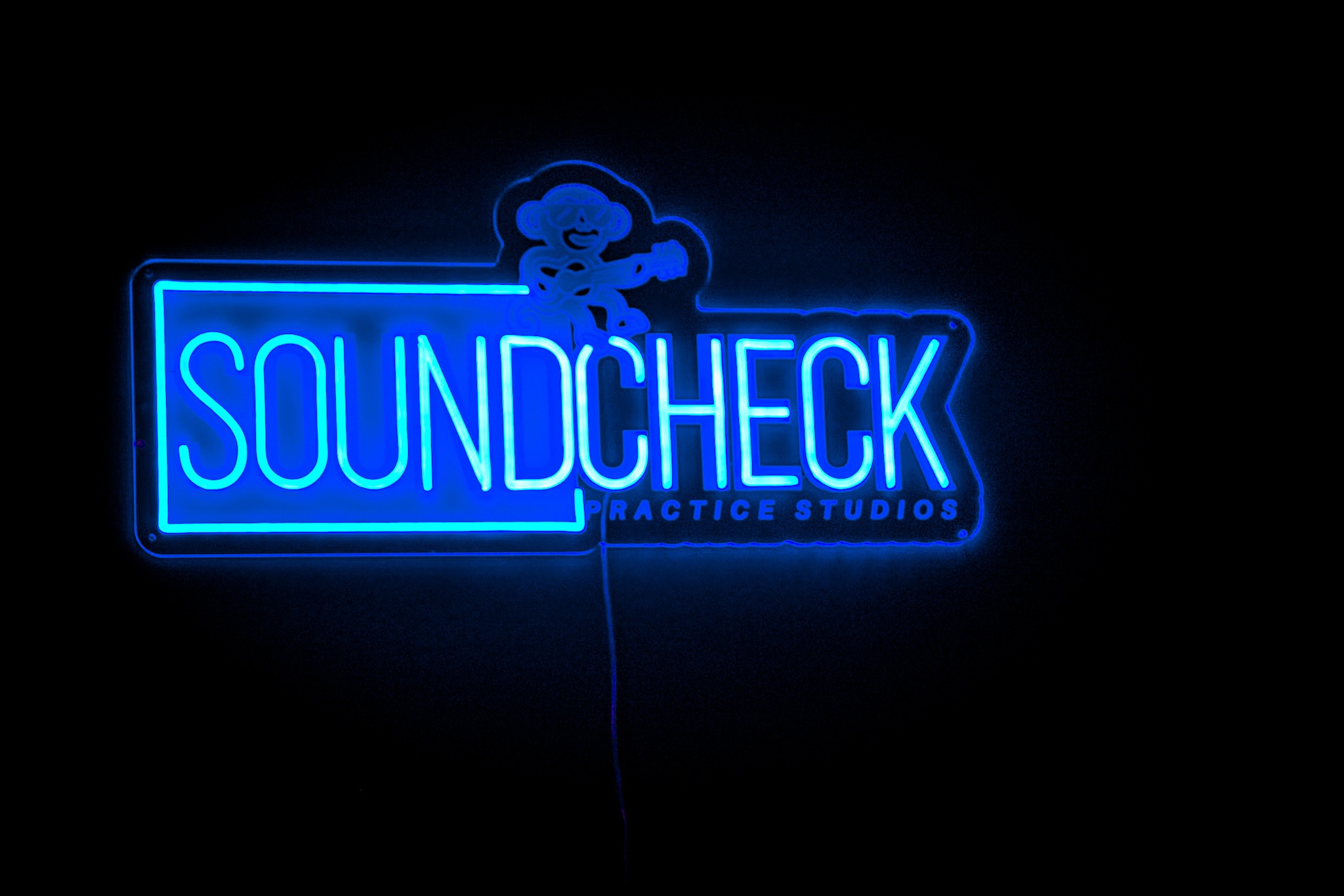 The blue SOUNDCHECK neon sign glowing on a dark wall