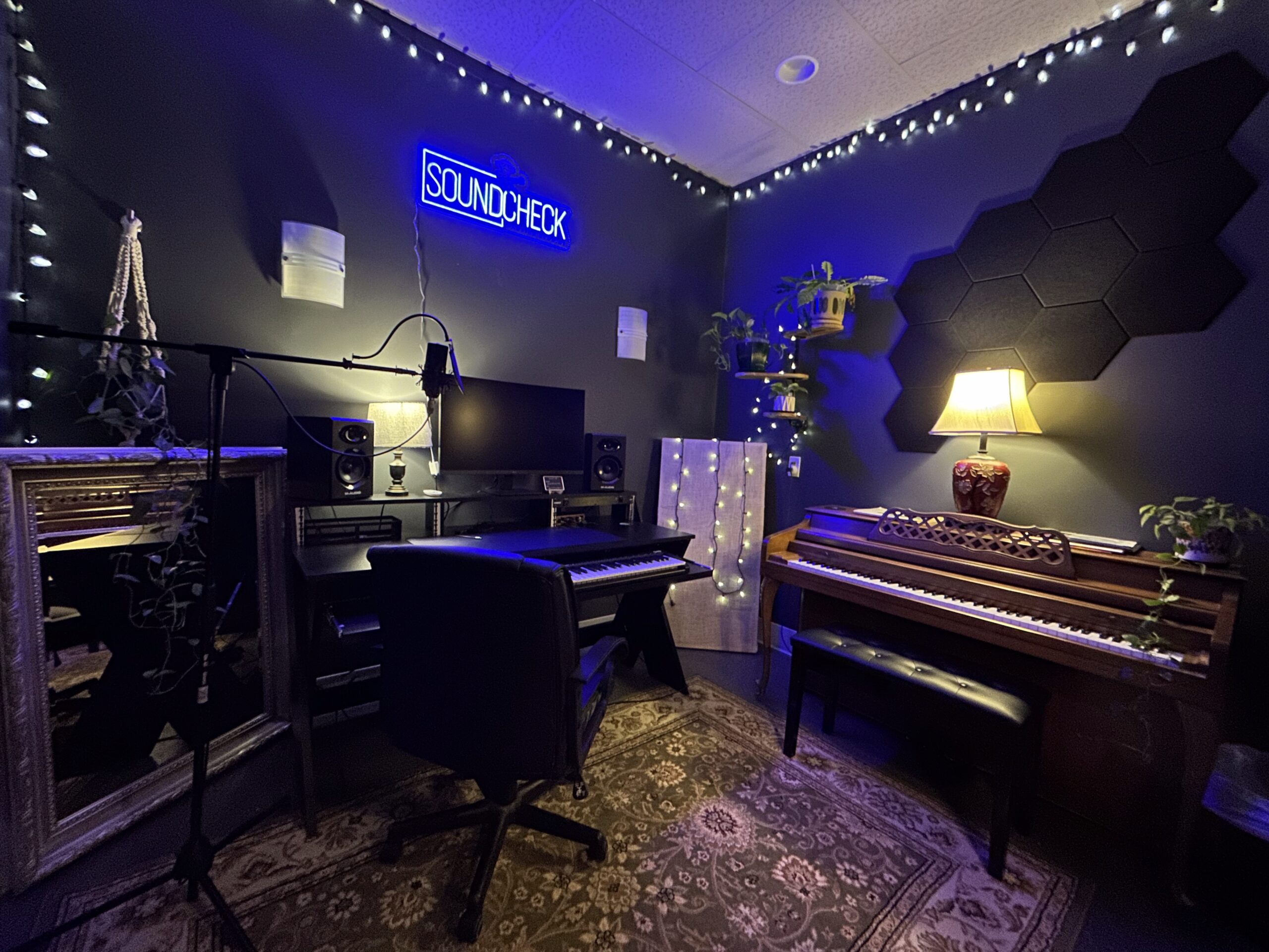 The Soundcheck recording room - studio monitors, a mic on a boom arm, and the vintage piano under the blue neon sign