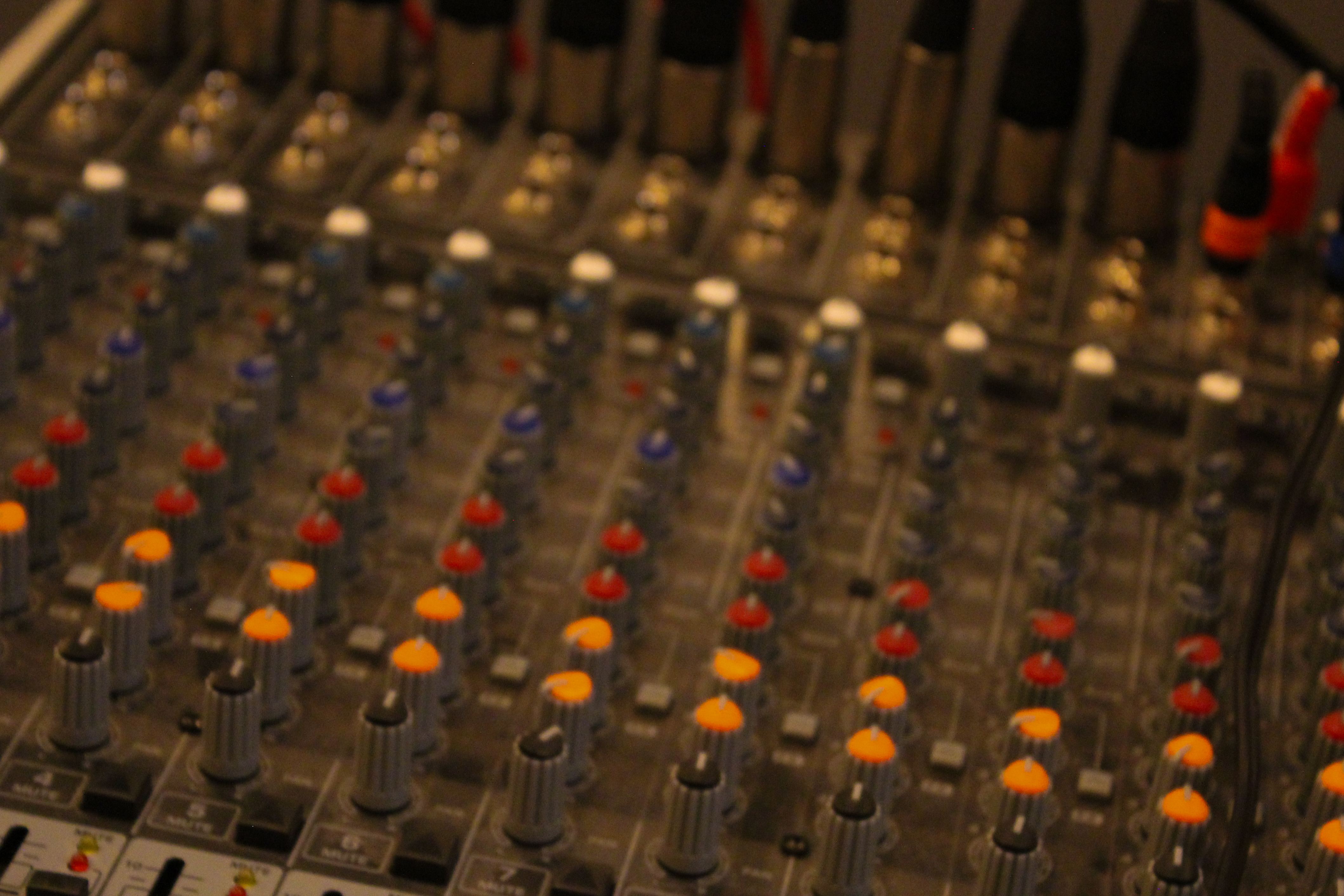 Close-up of an analog mixing console with rows of orange, red, and blue knobs and faders